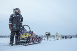 A guide stands with a harnessed husky team on a frozen river on the Arcora Husky Safari Experience in Muonio, Lapland.