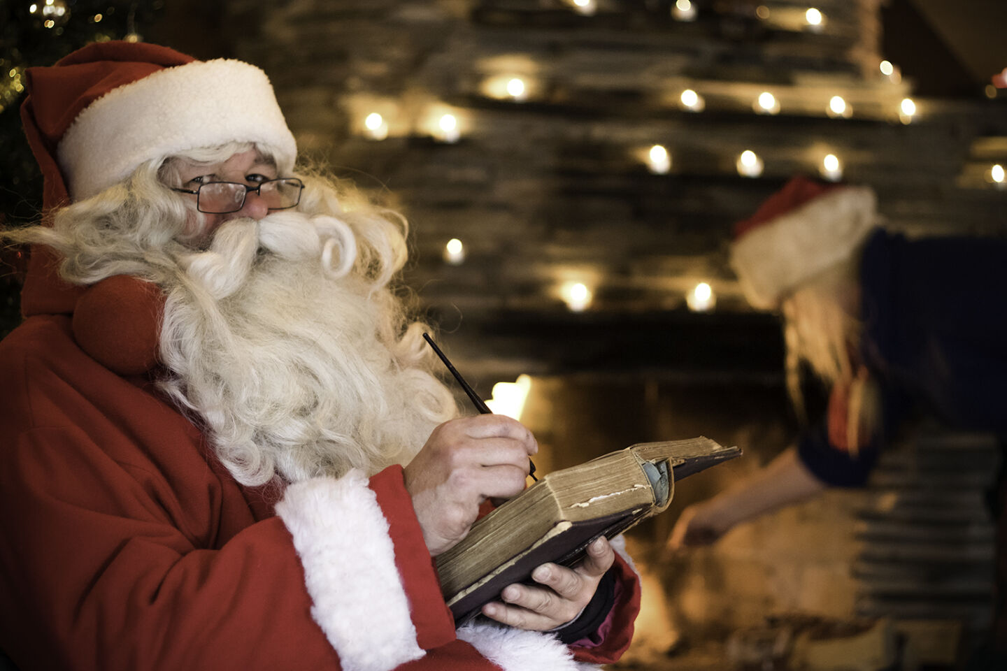Santa Claus writes in his old book by the fire in his cabin, a Christmas visit for Arcora guests in Muonio, Lapland.