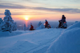 Snowmobilers stop on a fell top to watch the sunset on the Arcora Snowmobiling Safari in Muonio, Finnish Lapland.