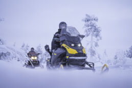 Two snowmobiles ride through snow-laden forest on the Arcora Snowmobiling Safari in Muonio, Finnish Lapland.