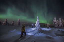 Two snowshoers with headlamps cross deep snow under the northern lights in the fells near Arcora, Muonio, Lapland.