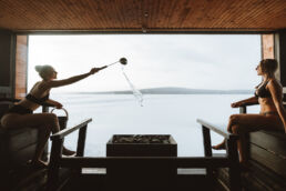 A guest throws water on the stones in a panorama sauna above a frozen lake at Arctic Sauna World, Muonio, Finnish Lapland.