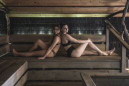 Two guests unwind on the wooden benches of a dark, dimly lit sauna at Arctic Sauna World in Muonio, Finnish Lapland.